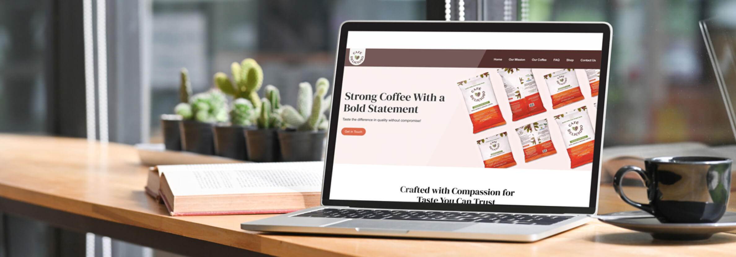 A laptop displays a Cafe Delicioso’s website, featuring product packaging and text, with a cup of coffee on a table alongside cacti.