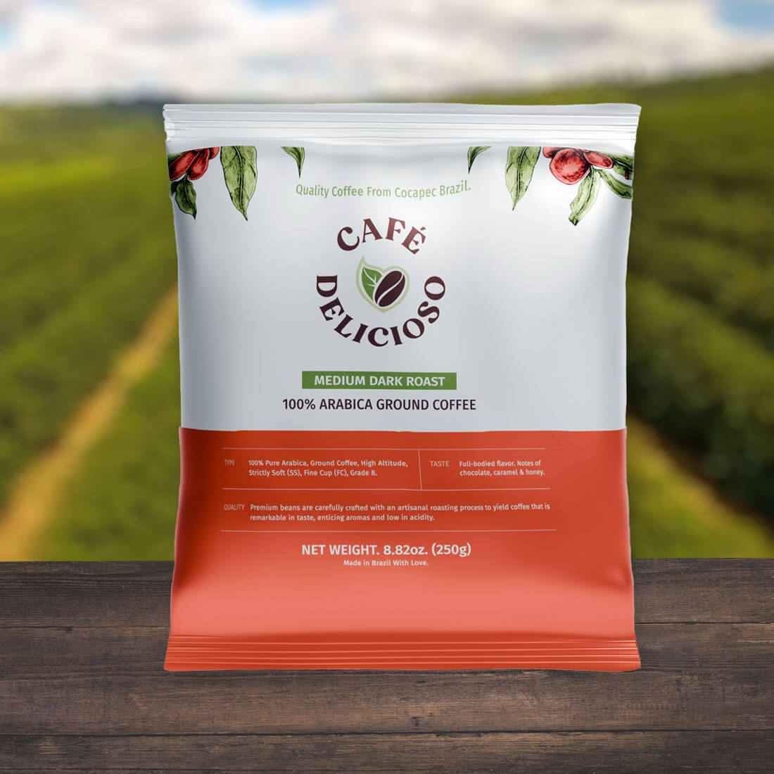 A bag of Café Delicioso coffee on top of a dark wood table, sitting in front of a field of greens.