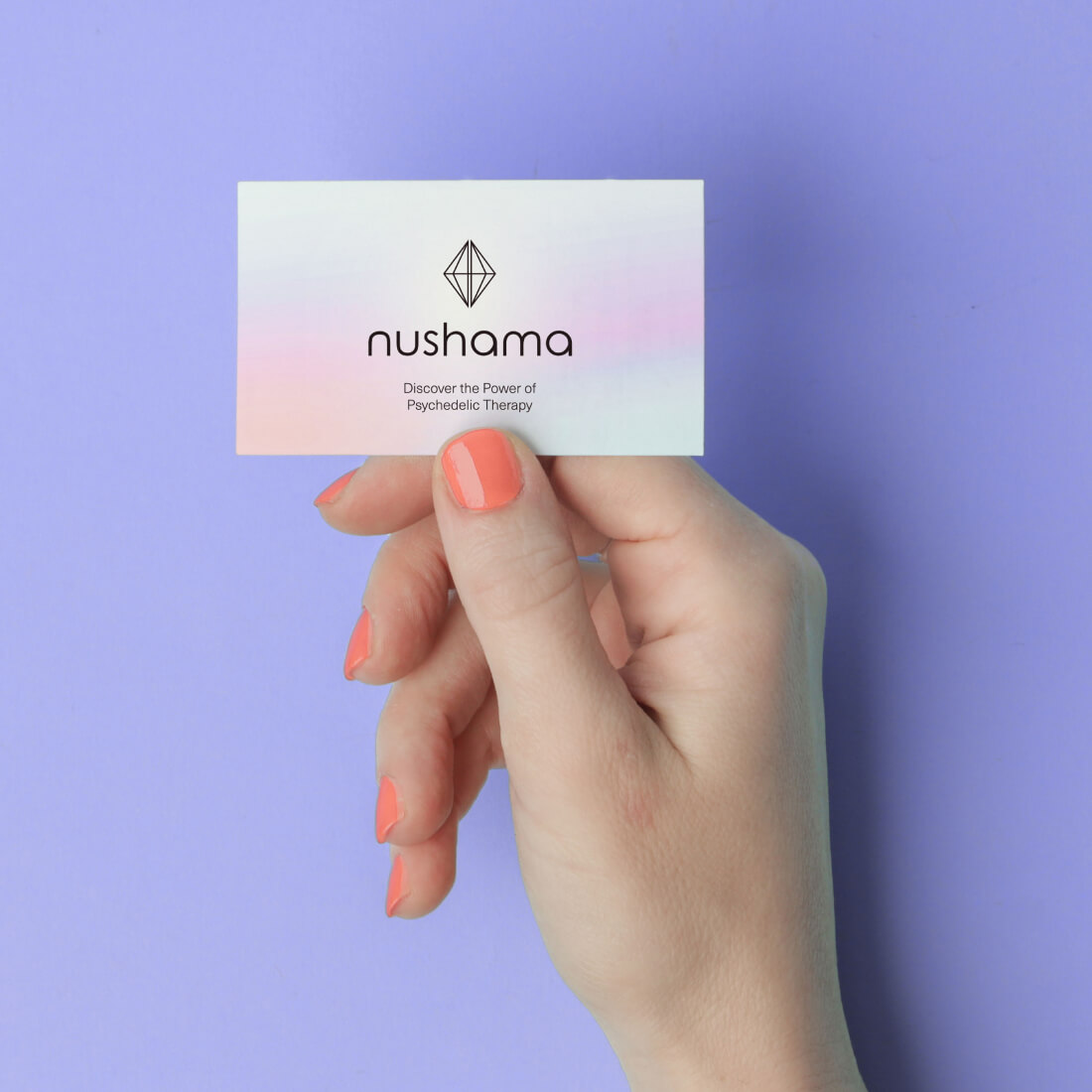 A hand holding a business card for Nushama, promoting psychedelic therapy, against a pastel purple background.