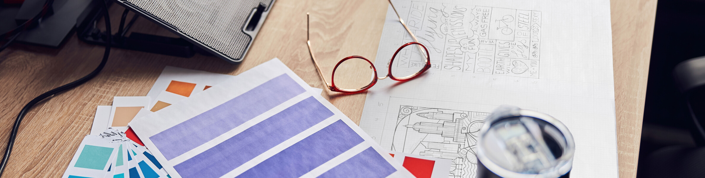A wooden desk with color swatches, sketches, and reading glasses, suggesting a creative workspace.
