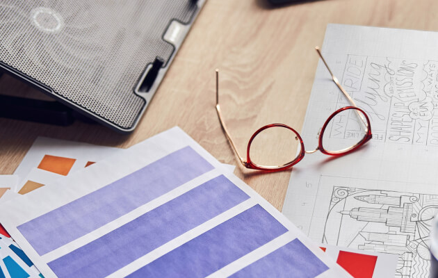A wooden desk with color swatches, sketches, and reading glasses, suggesting a creative workspace.