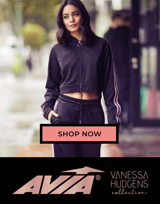 Vanessa Hudgens models a stylish black athleisure outfit with white stripes on a rainy street, promoting the AVIA Vanessa Hudgens collection with its logo and “shop now” button.