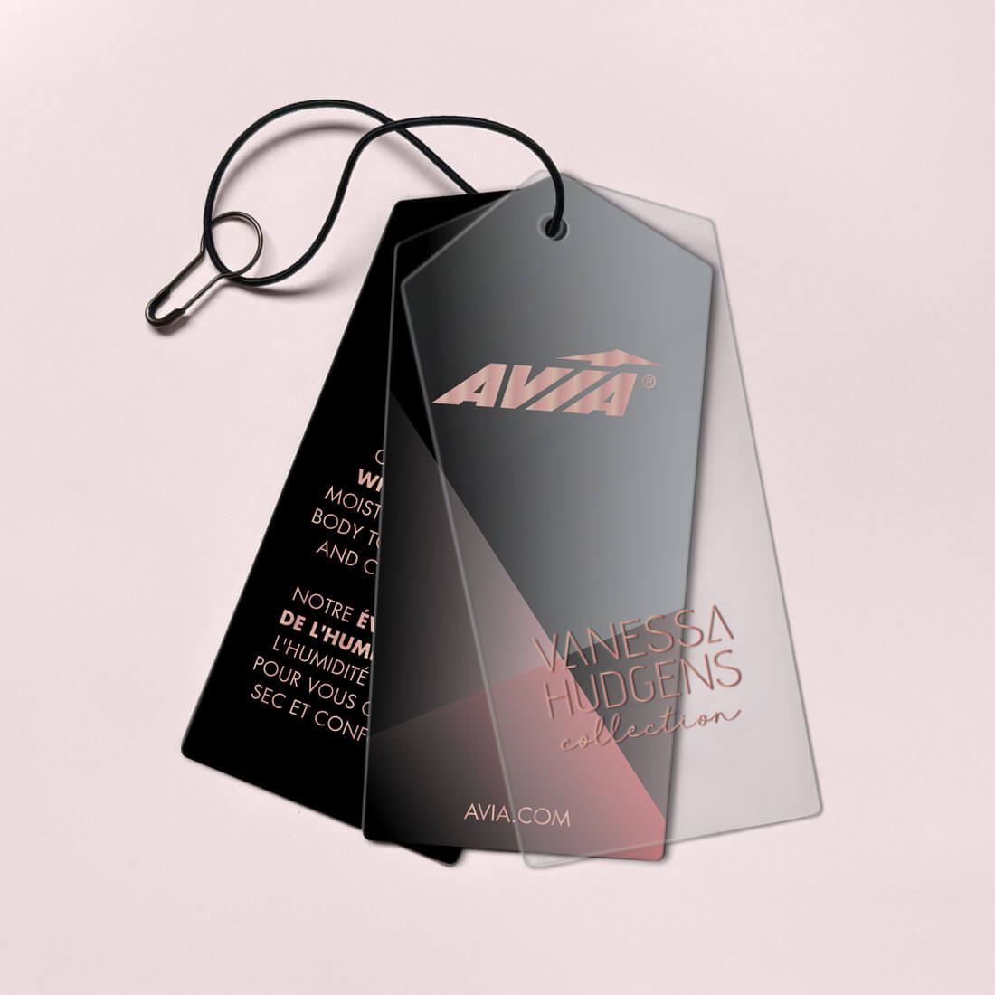 Two black hangtags with "AVIA" and "VANESSA HUDGENS collection" branding, on a light pink background.
